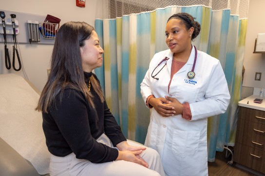Doctor converses with patient seated on exam table in exam room.
